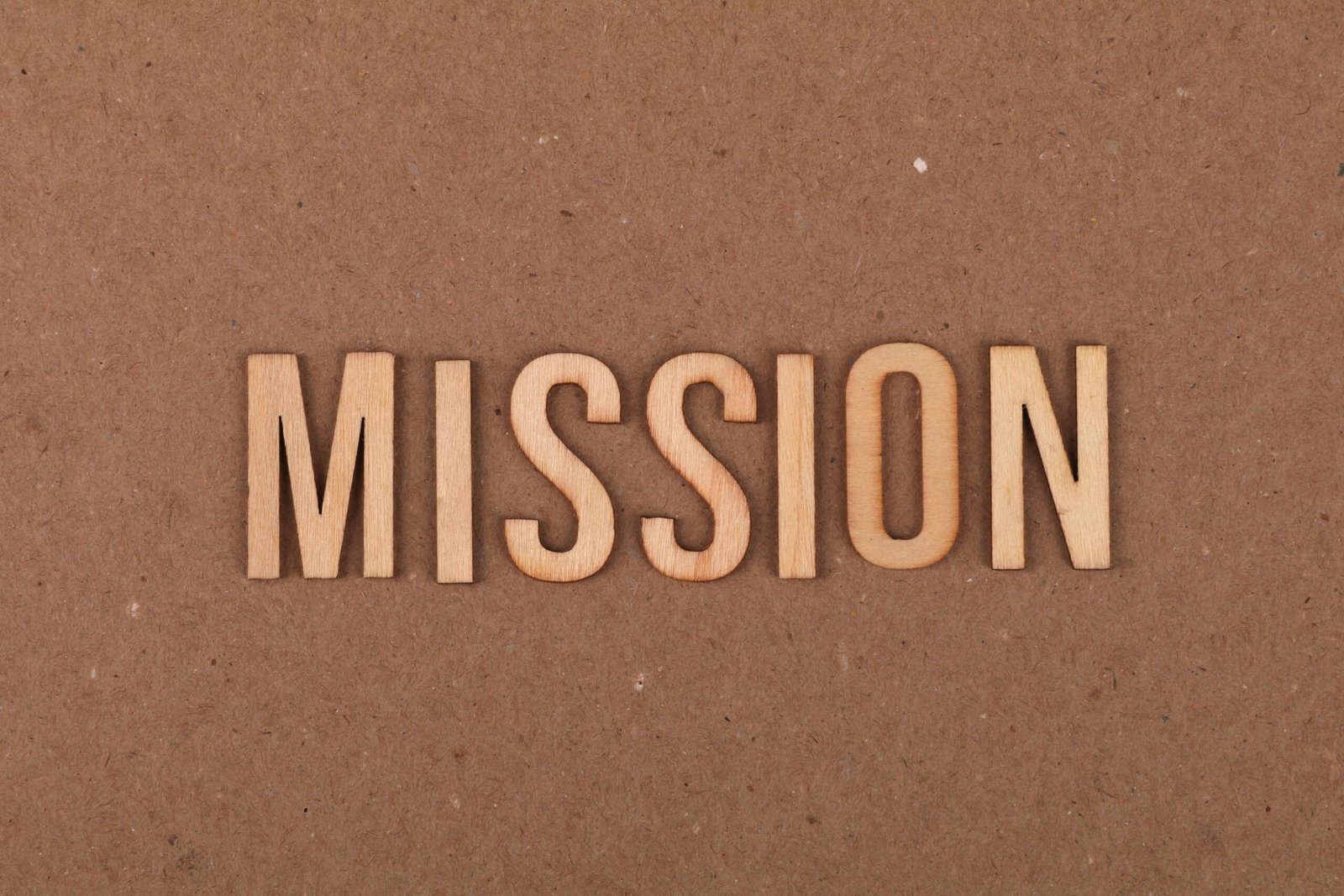 Wooden letters spelling 'MISSION' on textured cardboard background, emphasizing goals and purpose.